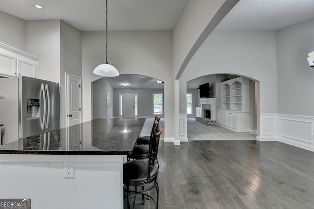 kitchen featuring a high ceiling, white cabinetry, stainless steel fridge with ice dispenser, a kitchen island, and dark wood-style floors