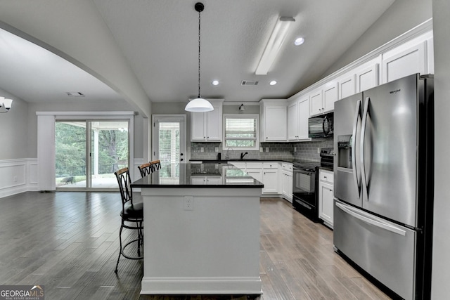 kitchen with a sink, dark countertops, visible vents, black appliances, and a kitchen island