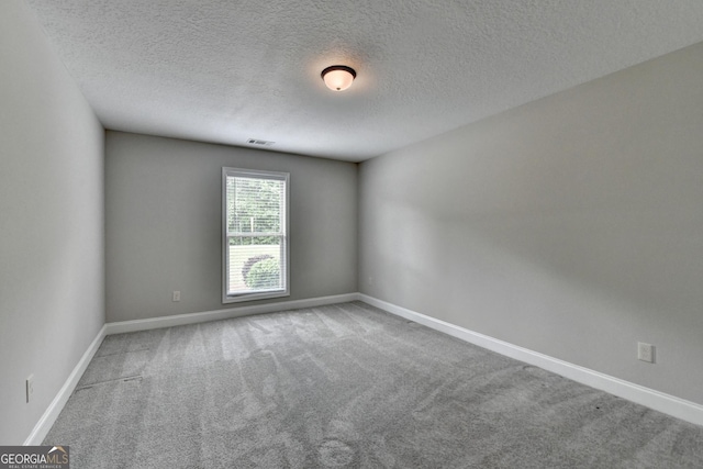 spare room with carpet flooring, a textured ceiling, visible vents, and baseboards