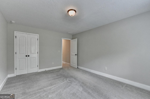 unfurnished bedroom with carpet flooring, a closet, a textured ceiling, and baseboards