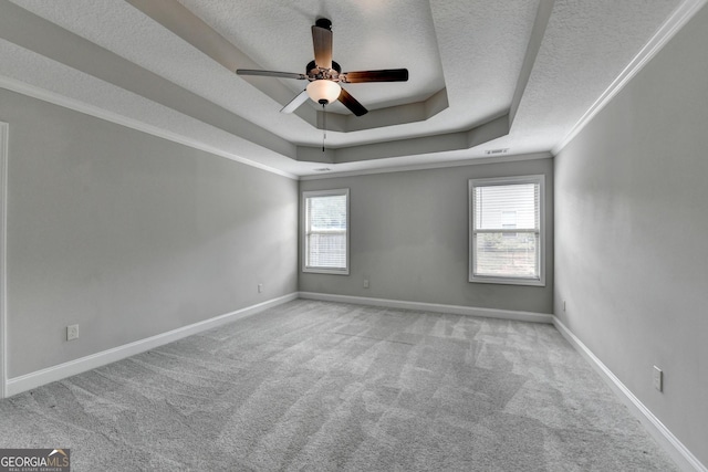 carpeted spare room featuring a ceiling fan, a tray ceiling, a textured ceiling, baseboards, and crown molding