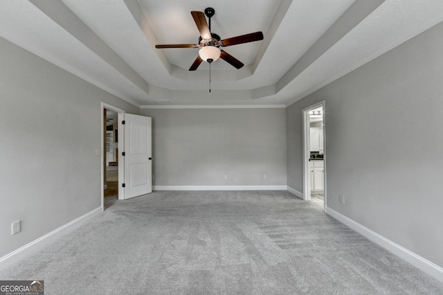 carpeted spare room with a tray ceiling, ceiling fan, and baseboards