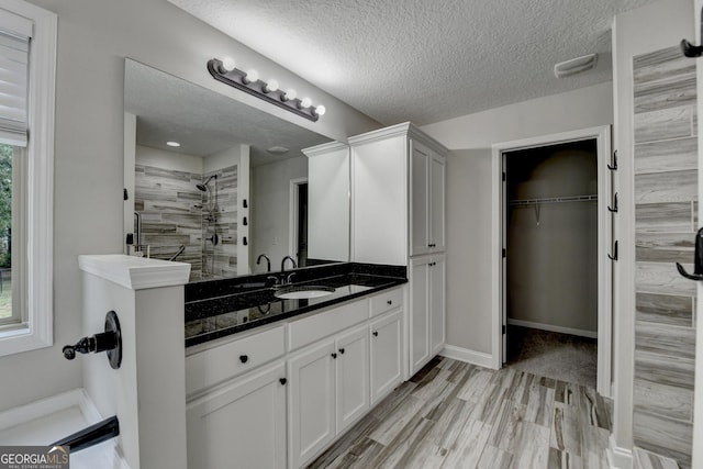 full bathroom featuring wood finished floors, vanity, a textured ceiling, a spacious closet, and a tile shower
