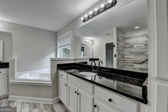 full bath with a bath, tiled shower, vanity, and a textured ceiling