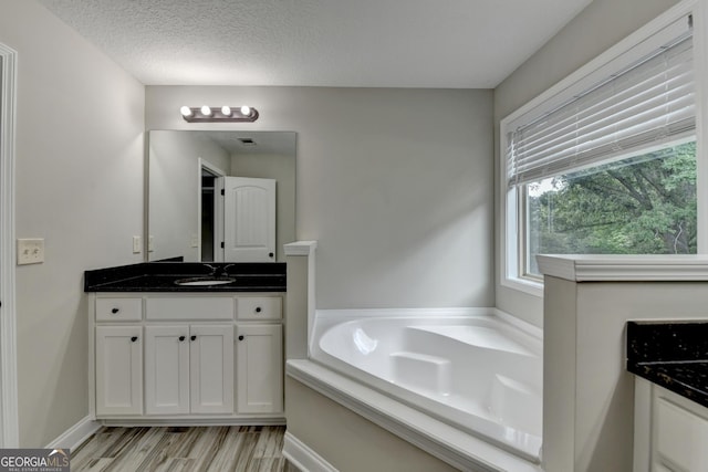 bathroom featuring a garden tub, wood finished floors, a textured ceiling, visible vents, and vanity