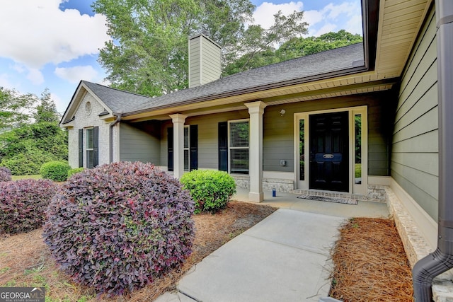 doorway to property with a porch, roof with shingles, and a chimney