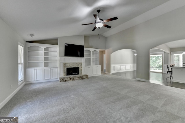 unfurnished living room with arched walkways, a ceiling fan, carpet, and built in shelves