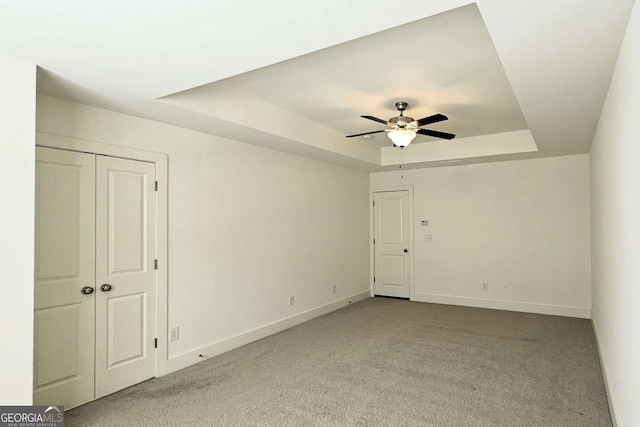 carpeted spare room featuring a tray ceiling, baseboards, and ceiling fan