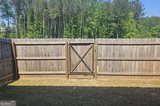 view of gate featuring a fenced backyard and a lawn