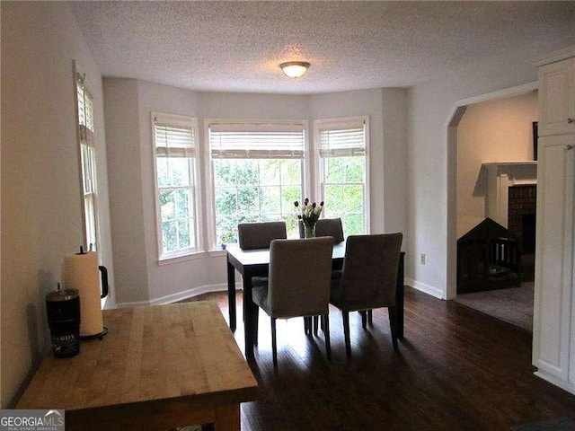 dining space featuring dark wood-style flooring, a textured ceiling, baseboards, and arched walkways