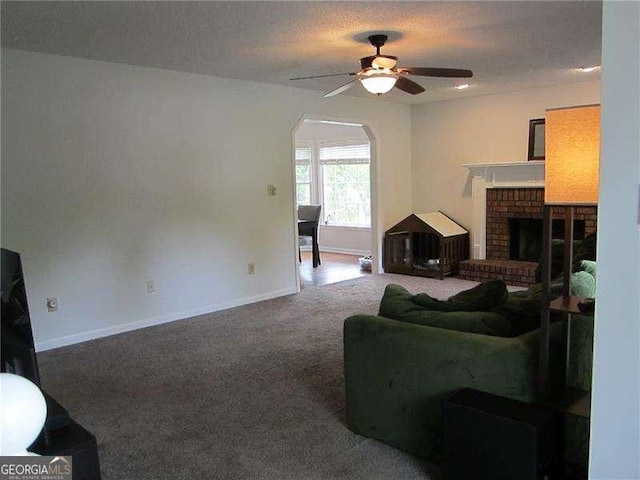 carpeted living area with a brick fireplace, arched walkways, a ceiling fan, and baseboards