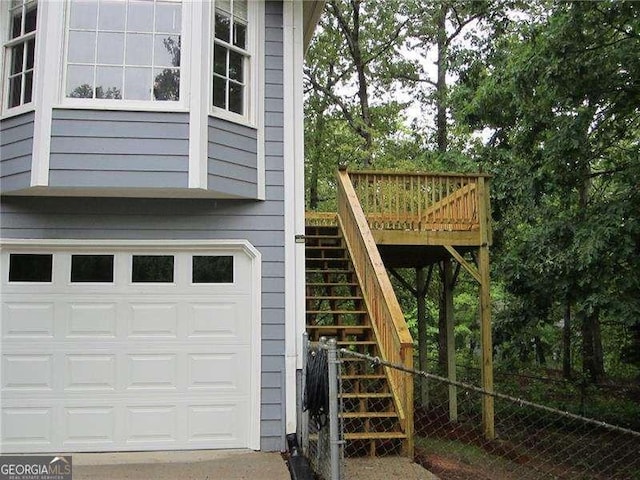 view of home's exterior with stairs, an attached garage, a deck, and fence