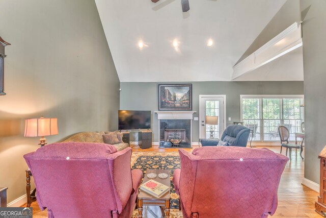 living area with high vaulted ceiling, a tile fireplace, baseboards, wood finished floors, and ceiling fan