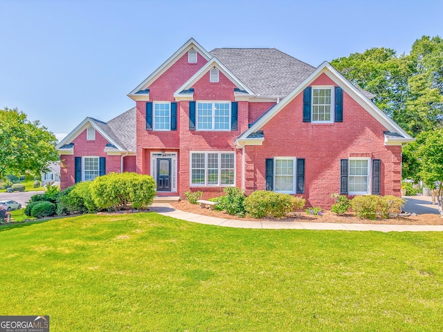 view of front of house with brick siding, a front yard, and roof with shingles