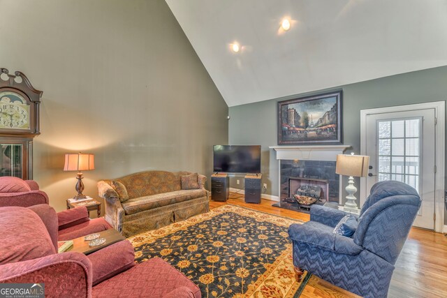 living area featuring high vaulted ceiling, a tiled fireplace, wood finished floors, and baseboards