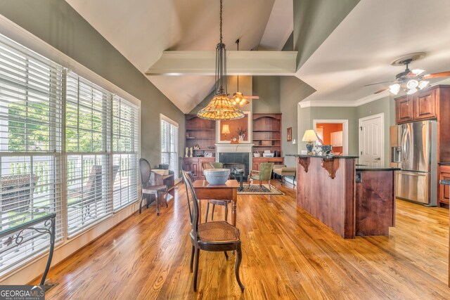 kitchen featuring stainless steel fridge, a ceiling fan, a fireplace, a breakfast bar area, and light wood-style floors