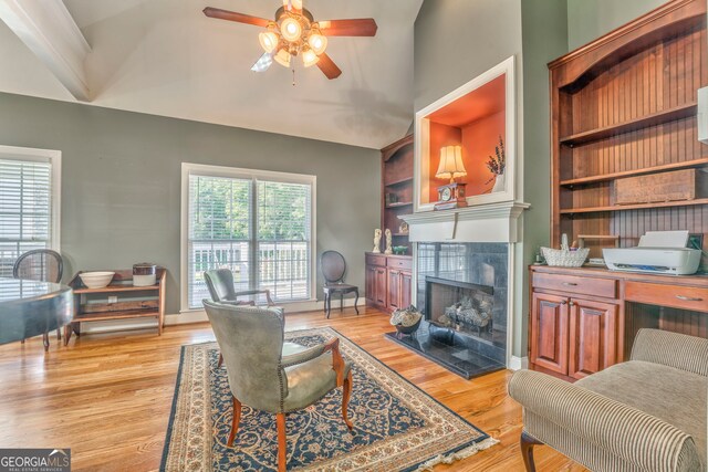 living area featuring a ceiling fan, lofted ceiling, a tile fireplace, light wood-style flooring, and built in shelves