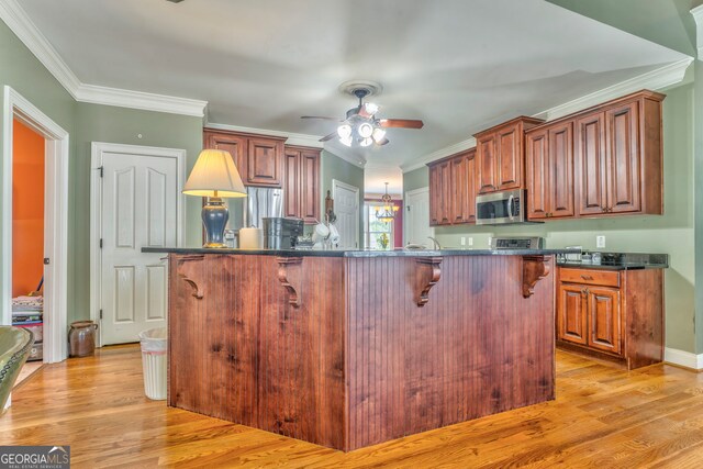 kitchen with stainless steel appliances, dark countertops, a ceiling fan, a breakfast bar, and ornamental molding