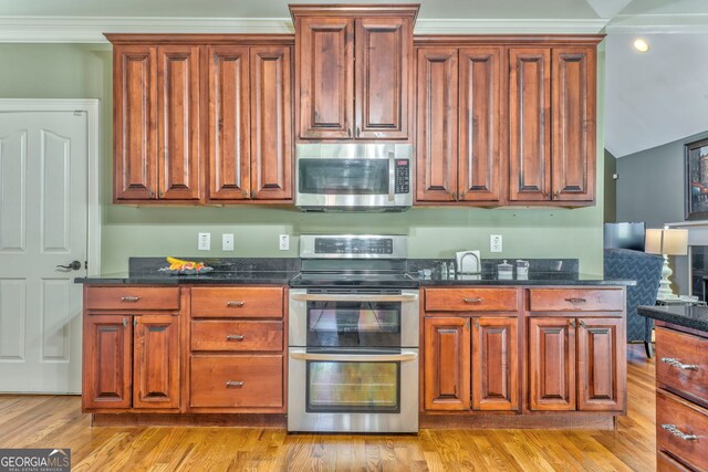 kitchen featuring appliances with stainless steel finishes, light wood-style flooring, dark stone counters, and brown cabinetry