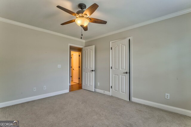unfurnished bedroom featuring baseboards, light colored carpet, crown molding, and a ceiling fan