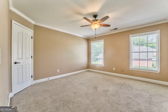 empty room with ornamental molding, a ceiling fan, plenty of natural light, baseboards, and carpet