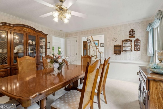 dining area featuring wallpapered walls, ornamental molding, stairs, a wainscoted wall, and light colored carpet