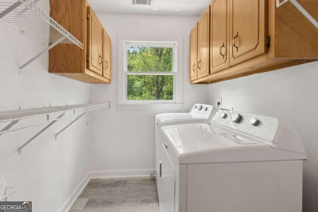 clothes washing area with cabinet space, visible vents, washing machine and clothes dryer, light wood-style flooring, and baseboards