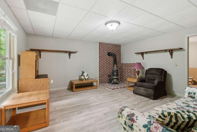 living area featuring a paneled ceiling, a wood stove, baseboards, and wood finished floors