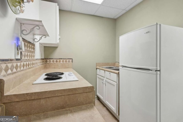 kitchen with a sink, a paneled ceiling, white cabinetry, white appliances, and light countertops