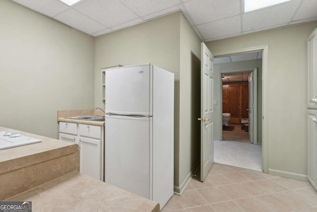 kitchen with freestanding refrigerator, light countertops, light tile patterned floors, a paneled ceiling, and baseboards
