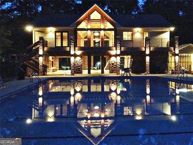 back of house at night with a balcony, a patio area, and stairs