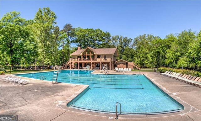 community pool featuring view of wooded area and a patio