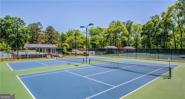 view of tennis court with community basketball court, fence, and view of wooded area