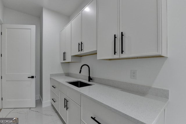 kitchen with white cabinetry, baseboards, marble finish floor, and a sink
