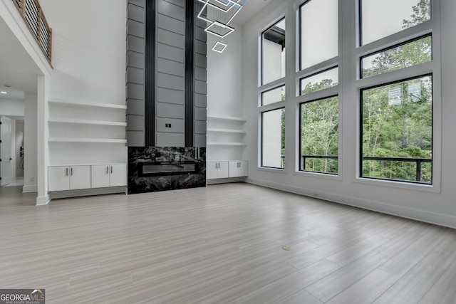 unfurnished living room with wood finished floors, a towering ceiling, visible vents, a fireplace, and baseboards