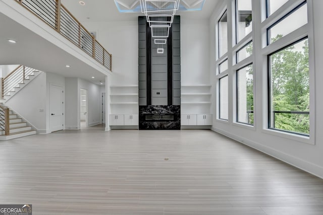 unfurnished living room with wood finished floors, baseboards, a high ceiling, and stairs