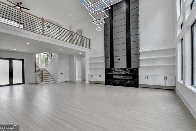 unfurnished living room with stairs, a high ceiling, baseboards, and french doors