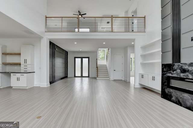 unfurnished living room featuring light wood-style flooring, baseboards, visible vents, ceiling fan, and a towering ceiling