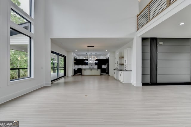 unfurnished living room with light wood finished floors, a high ceiling, baseboards, and recessed lighting