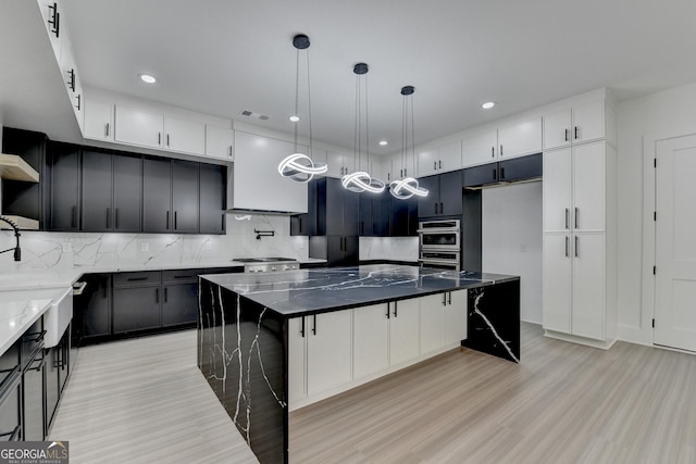 kitchen with backsplash, a spacious island, dark stone counters, and light wood-style floors