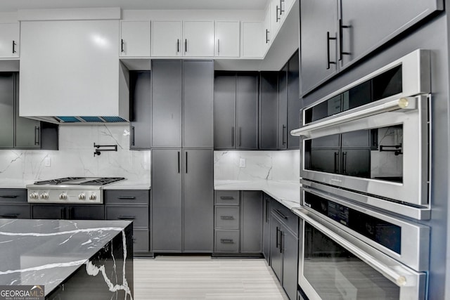 kitchen featuring stainless steel appliances, backsplash, and light stone counters