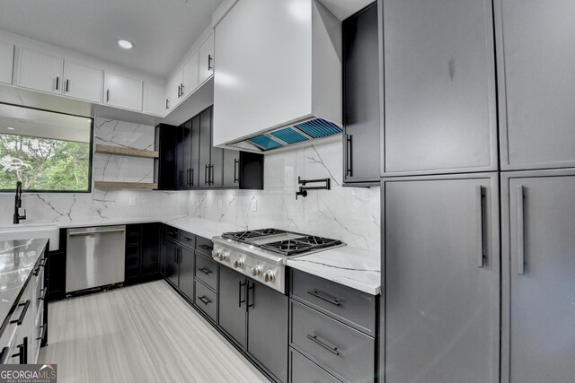 kitchen featuring a sink, light stone countertops, wall chimney range hood, appliances with stainless steel finishes, and tasteful backsplash