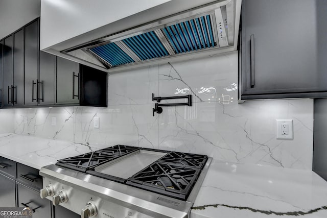 kitchen featuring backsplash, light stone countertops, ventilation hood, and stovetop
