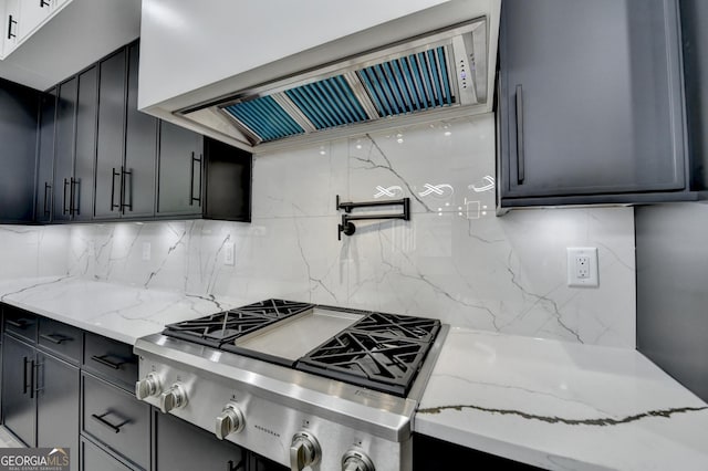 kitchen with tasteful backsplash, light stone counters, range hood, dark cabinetry, and cooktop
