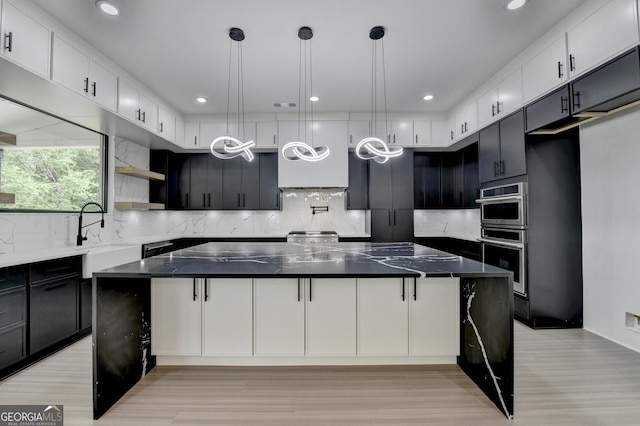 kitchen with a sink, tasteful backsplash, open shelves, a spacious island, and light wood-style flooring
