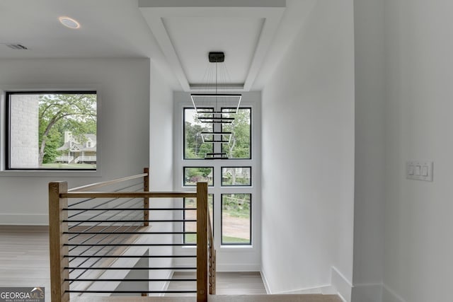 stairs featuring wood finished floors, visible vents, an inviting chandelier, a raised ceiling, and baseboards