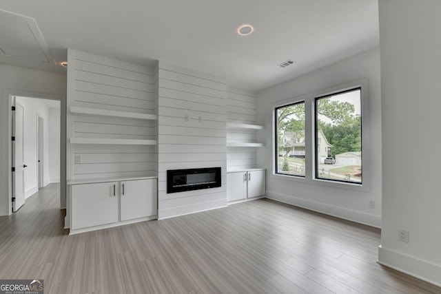 unfurnished living room with wood finished floors, attic access, a fireplace, visible vents, and baseboards