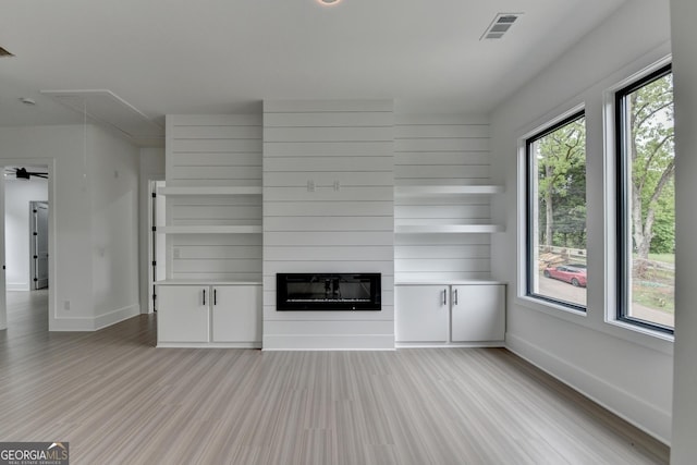 unfurnished living room featuring light wood-style flooring, attic access, baseboards, visible vents, and a large fireplace