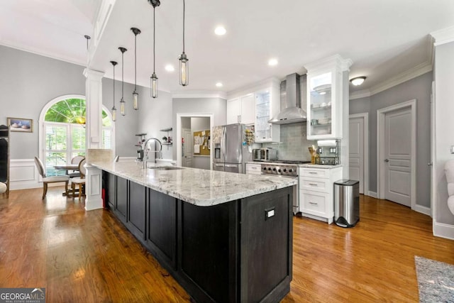 kitchen featuring a sink, wall chimney exhaust hood, white cabinetry, and appliances with stainless steel finishes