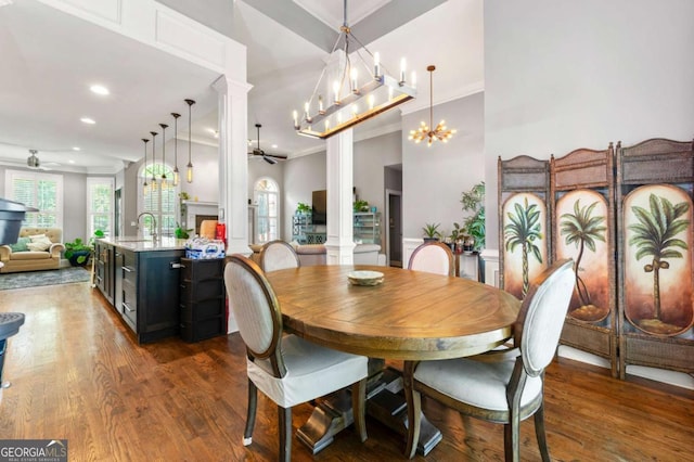 dining space with a healthy amount of sunlight, dark wood-type flooring, ceiling fan with notable chandelier, and ornate columns